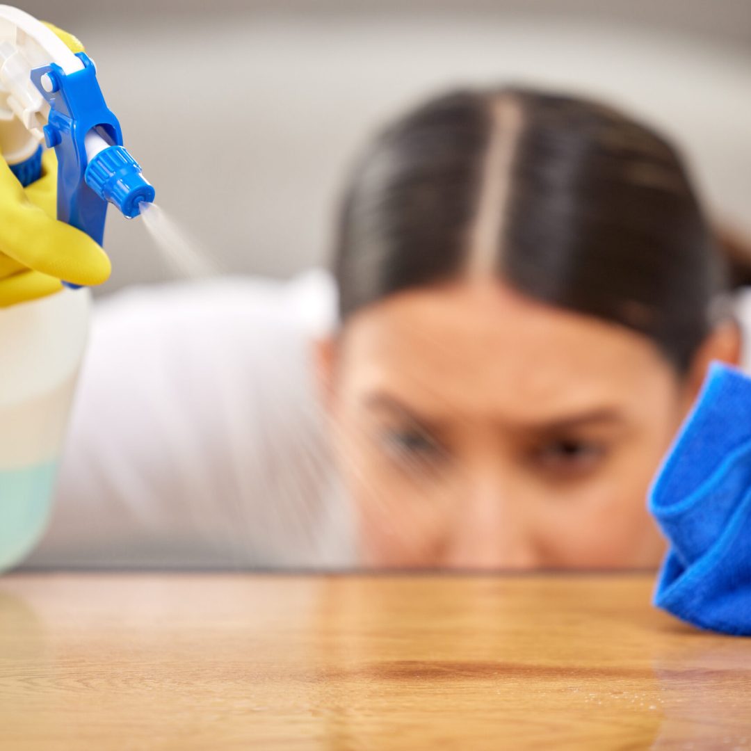 Shot of a young woman spraying cleaner on her coffee table.
