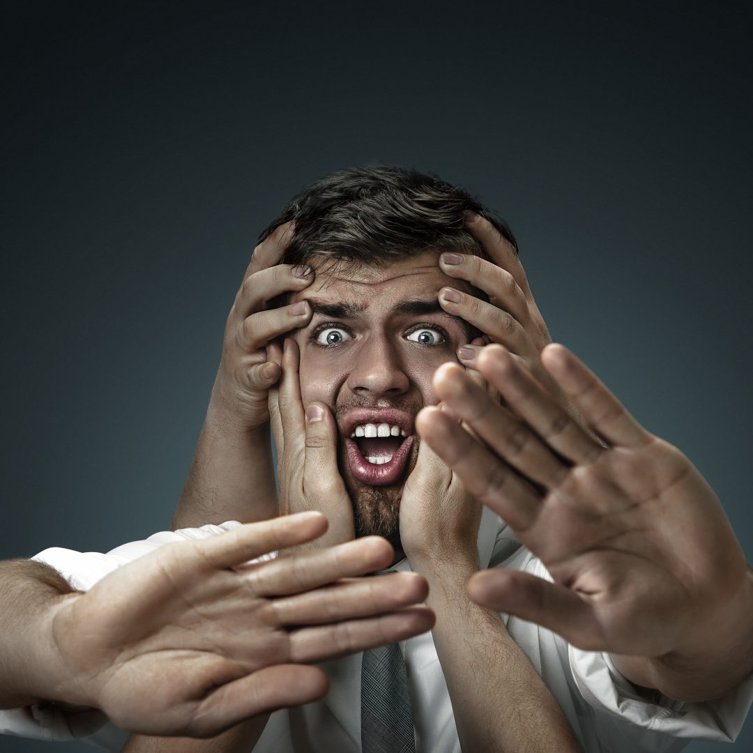 A male model surrounded by hands like his own thoughts on dark background. A young man doubts, can't choose the right decision and decide. Concept of mental problems, troubles in work, indecision.